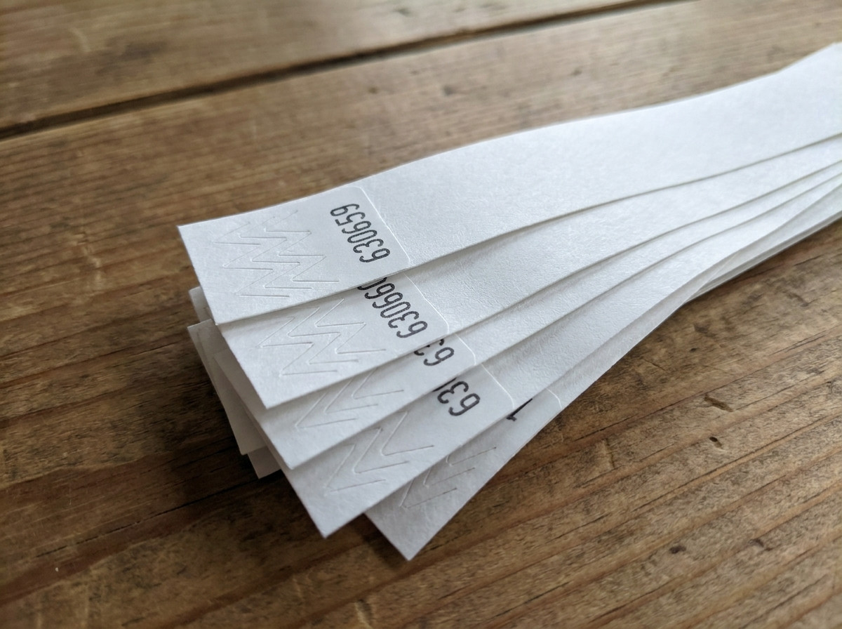 Primo piano su braccialetti Tyvek con numerazione sequenziale stampata in nero, disposti a ventaglio su un tavolo di controllo accessi durante un evento
